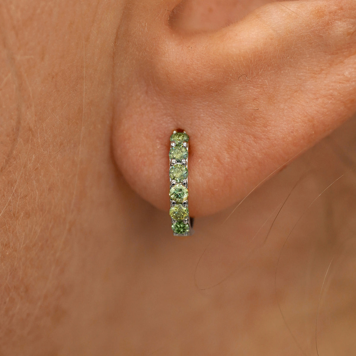 Close up view of a model's ear wearing a white gold Small Light Green Lab Diamond Huggie Hoop