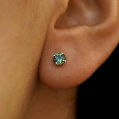 Close up view of a model's ear wearing a solid 14k gold green sapphire pressure lock earring