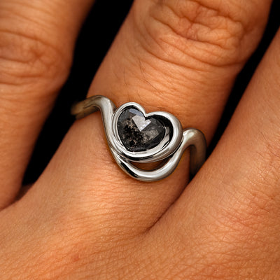 A model's hand wearing a 14k white gold Heart Salt and Pepper Diamond Infinite Wave Ring