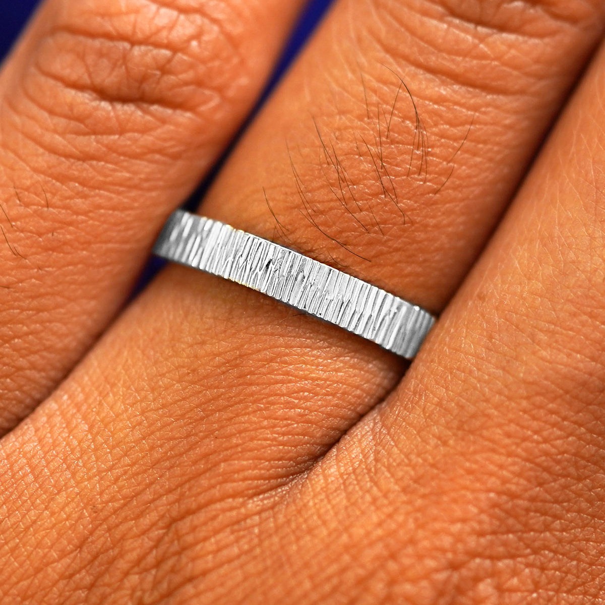 Close up view of a model's fingers wearing a 14k white gold Industrial Wood Band
