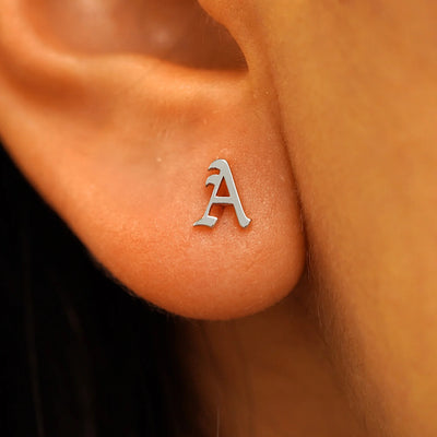 Close up view of a models ear wearing a 14k white gold gothic initial stud earring in the letter A