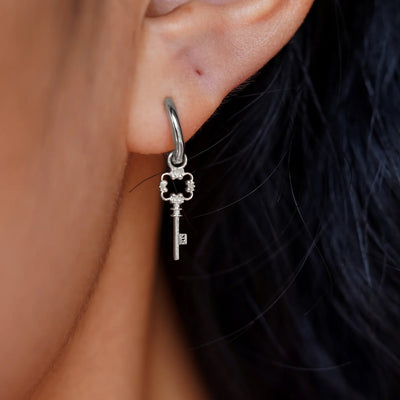 Close up view of a model's ear wearing a white gold Key Charm on a Curvy Huggie Hoop