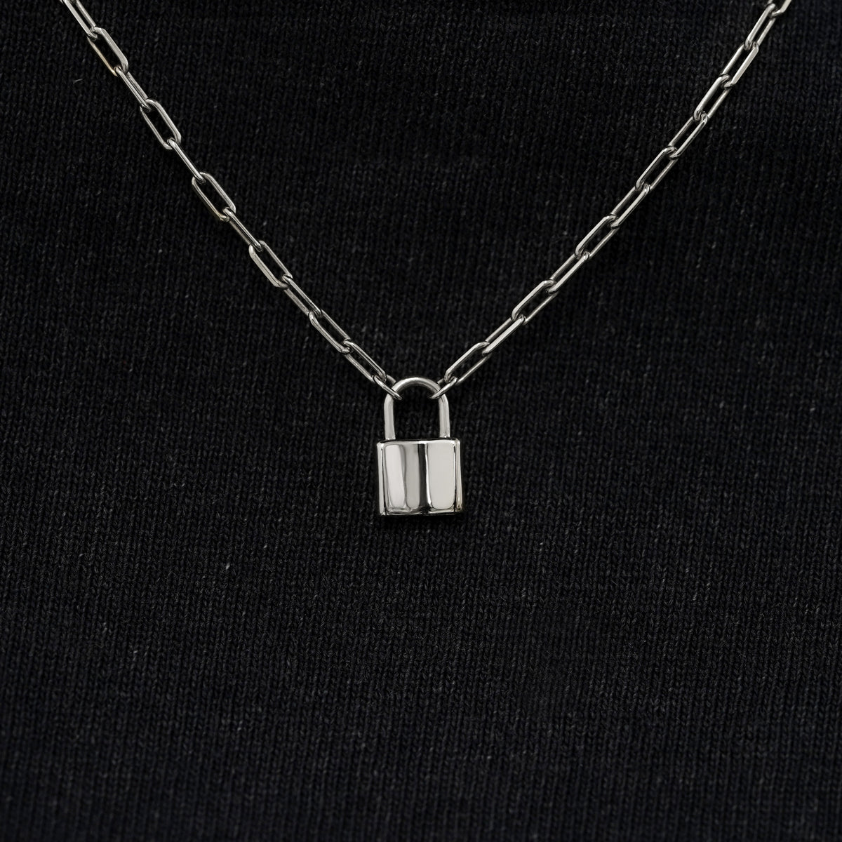 Close up view of a solid 14k white gold lock necklace against a model's black shirt