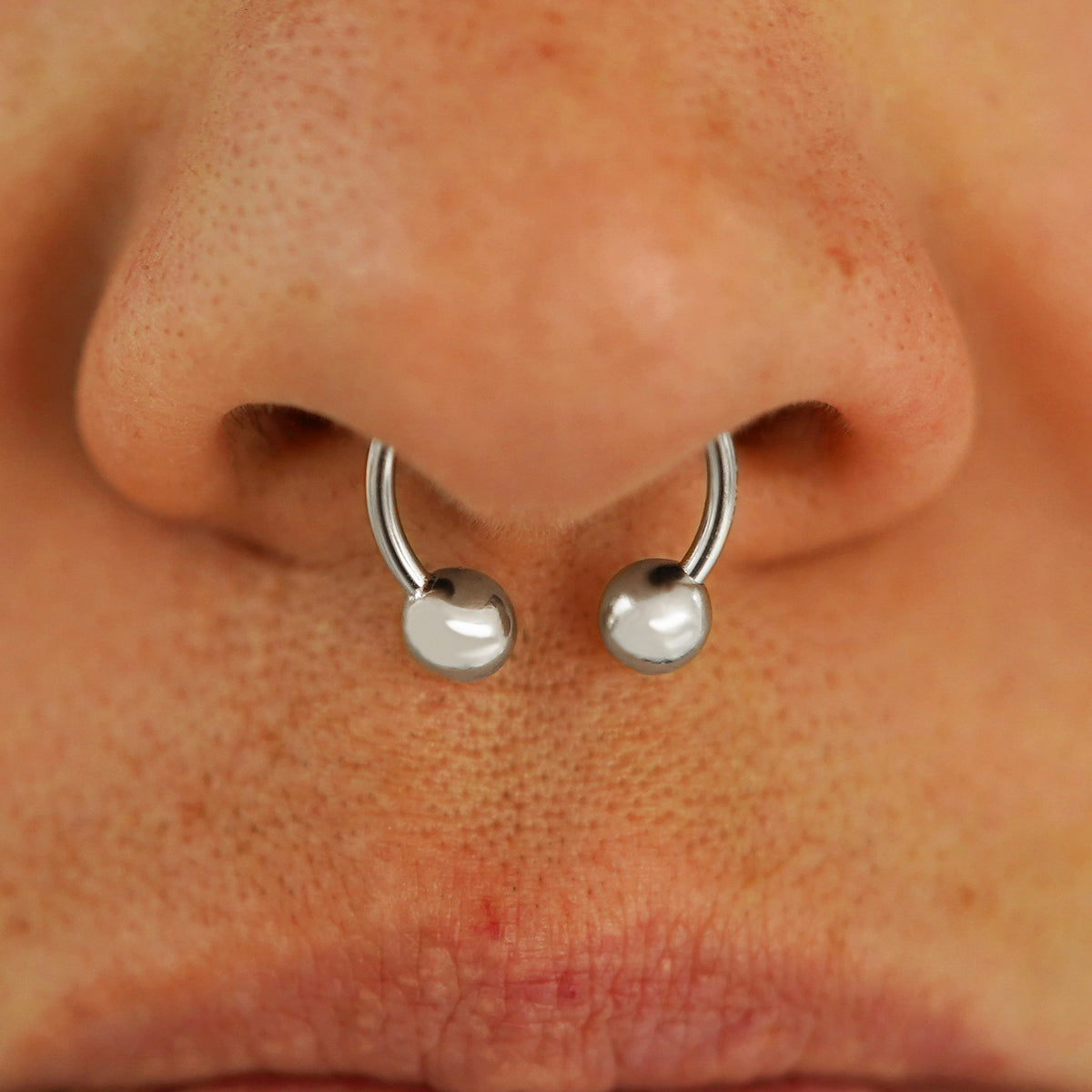 Close up view of a model's nose wearing a 14k white gold Medium Horseshoe in a septum piercing