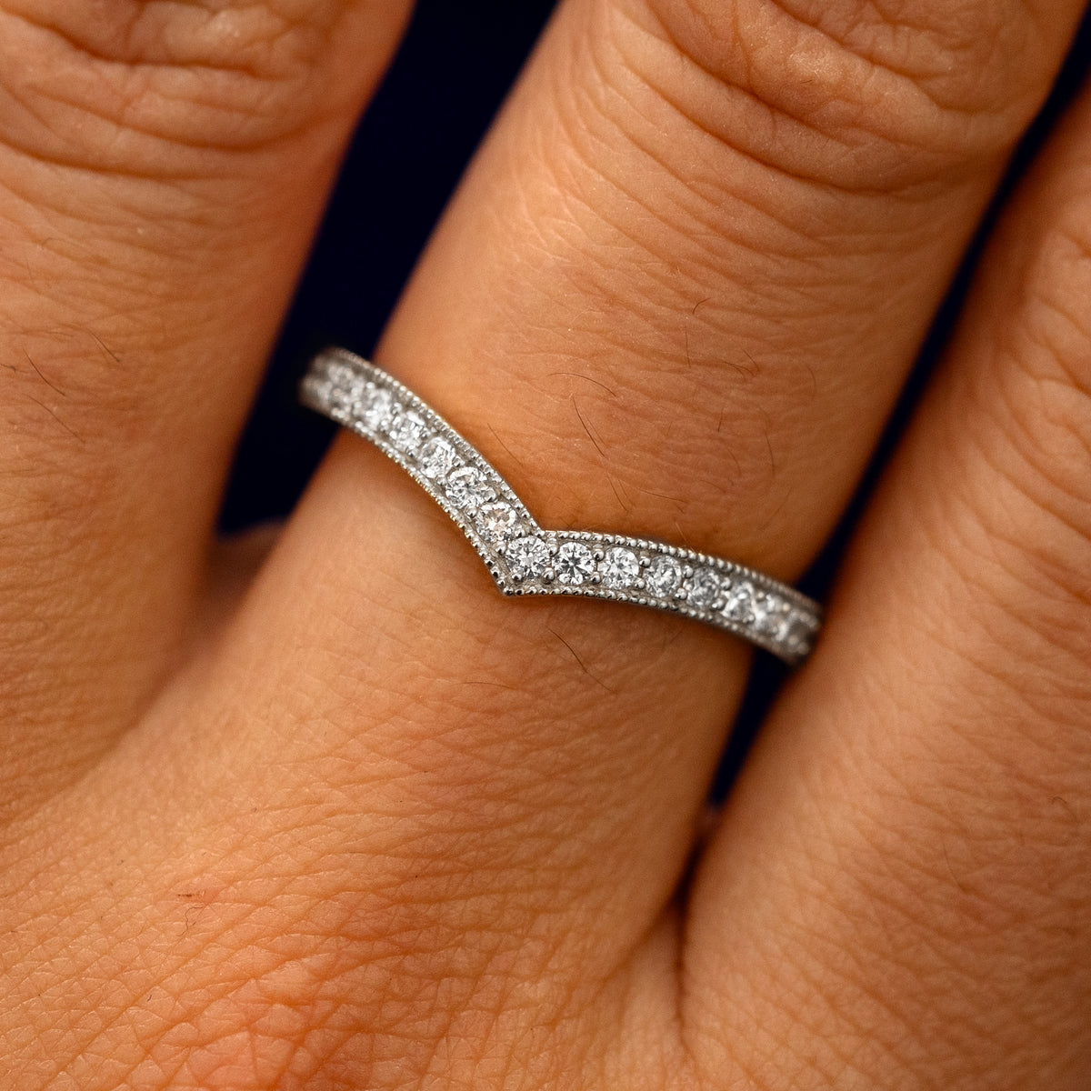 Close up view of a model's fingers wearing a 14k white gold Milgrain Pave Diamond Chevron Band