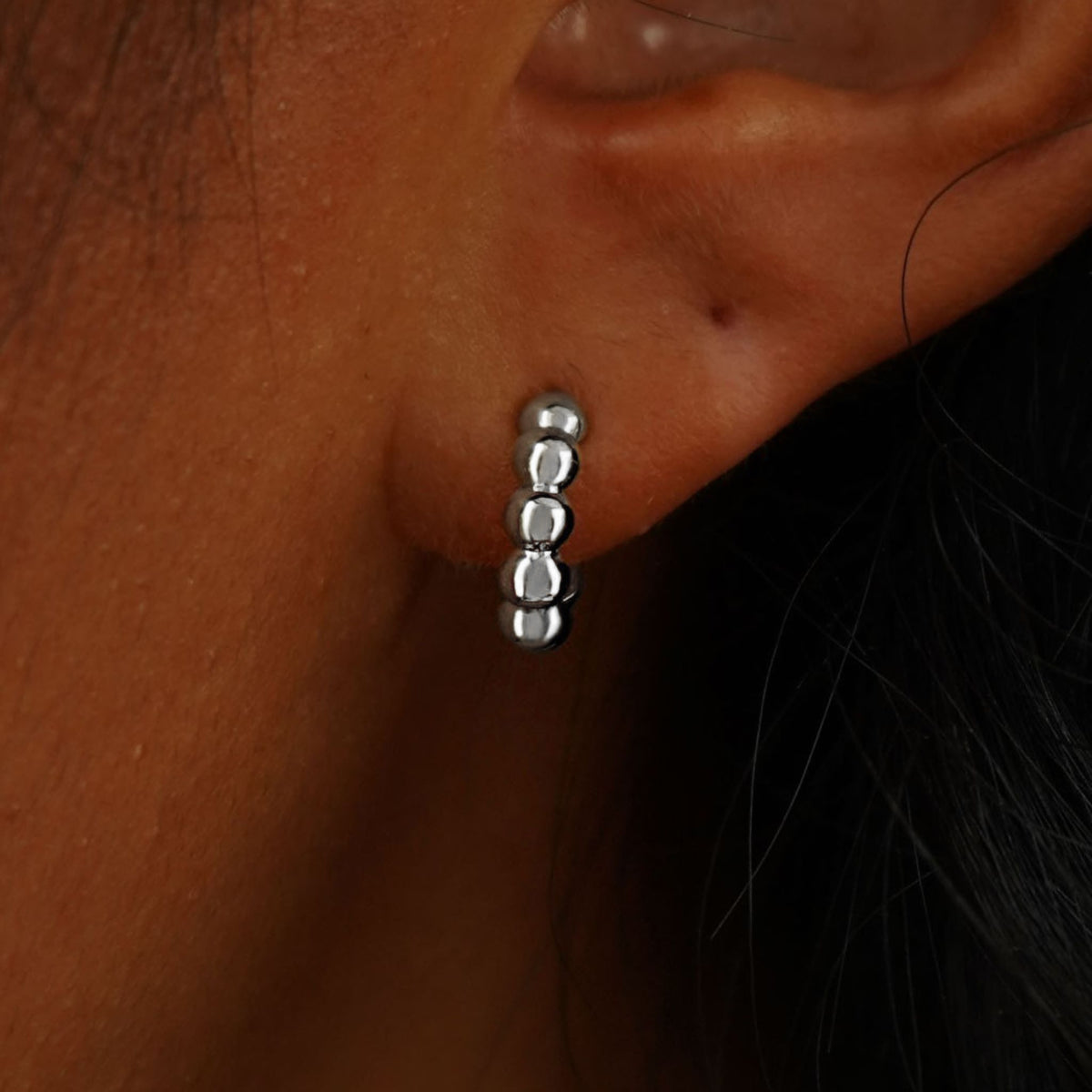 Close up view of a model's ear wearing a 14k white gold Mini Puffy Beaded Hoop