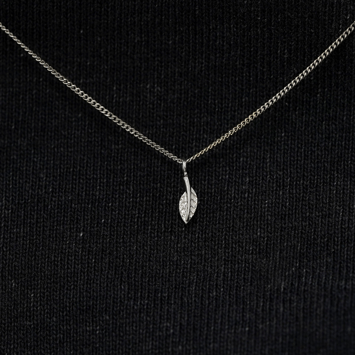 Close up view of a solid 14k white gold mini leaf necklace against a model's black shirt