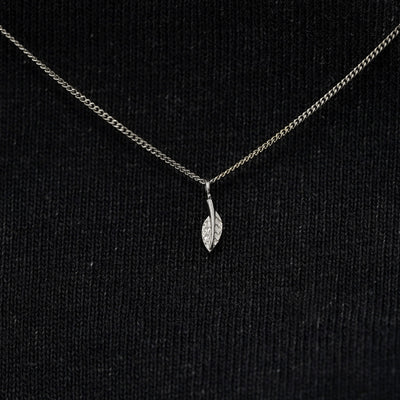 Close up view of a solid 14k white gold mini leaf necklace against a model's black shirt