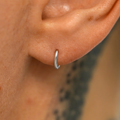 A model's ear wearing a 14k white gold Mini Seamless Huggie Hoop / Piercing