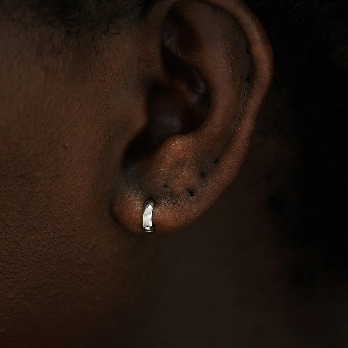 Close up view of a model's ear wearing a 14k white gold Mini Wide Huggie Hoop Earring