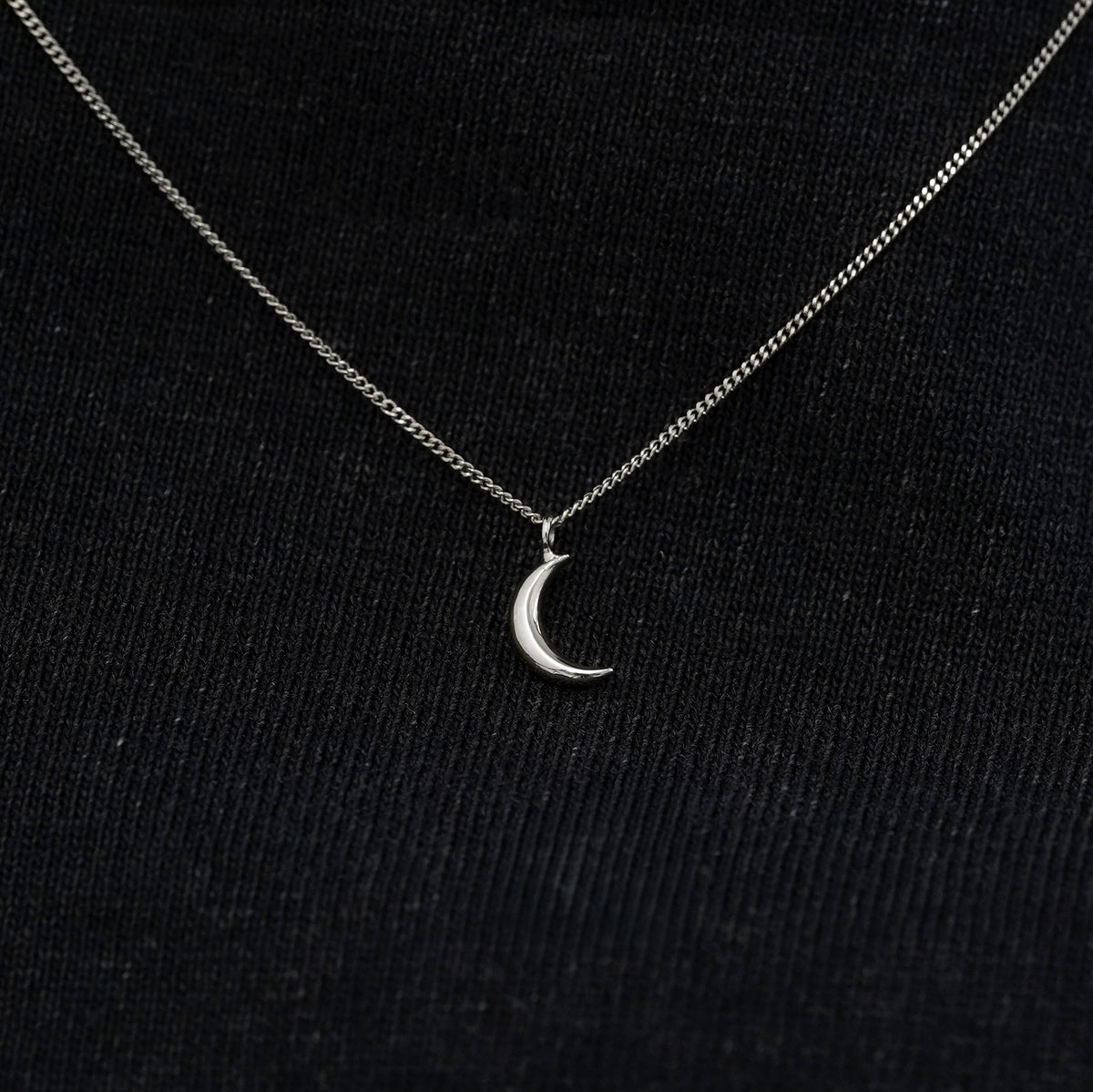 Close up view of a solid 14k white gold moon necklace against a model's black shirt