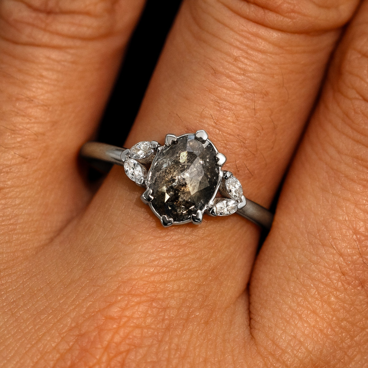 A model's hand wearing a 14k white gold Oval Salt and Pepper Diamond Heart Prong Ring