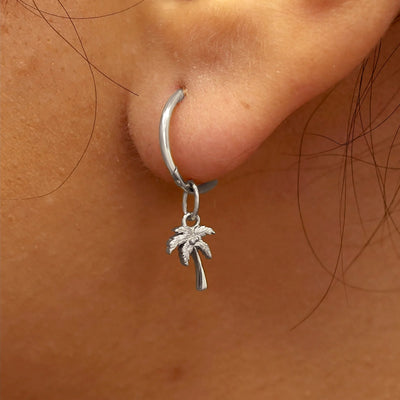 Close up view of a model's ear wearing a white gold Palm Tree Charm on a Small Seamless Huggie Hoop