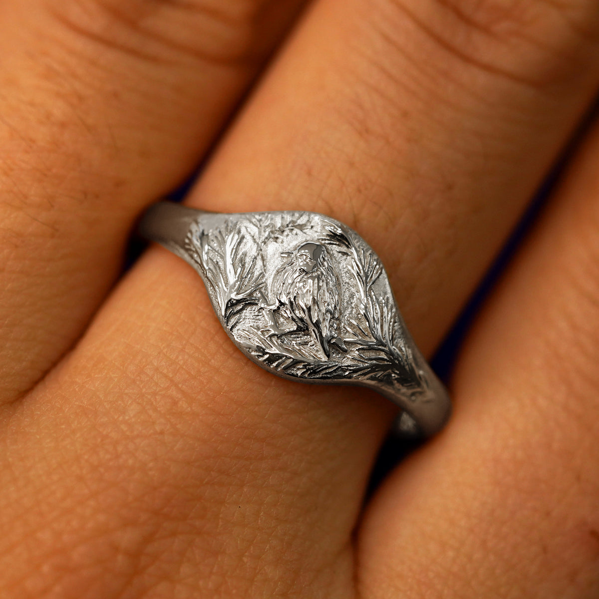 Close up view of a model's fingers wearing a 14k white gold Pine and Bird Signet Ring