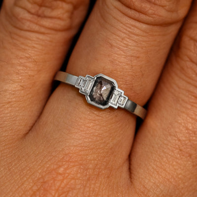 Close up view of a model's hand wearing a 14k white gold Emerald Cut Salt and Pepper and Clear Baguette Diamond Ring