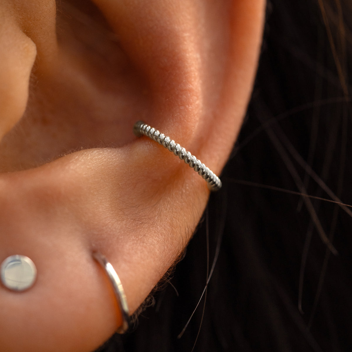 A close up of someone's ear with a 14k white gold rope cuff attached on their  outer ear.