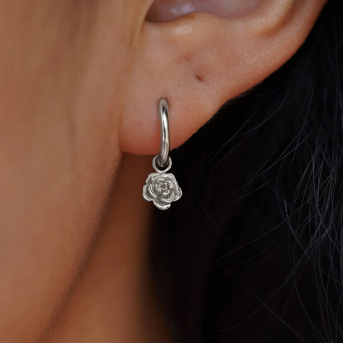 Close up view of a model's ear wearing a white gold Rose Charm on a Small Curvy Huggie Hoop