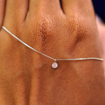 A solid white gold Rose Quartz Necklace draped across the back of a model's hand