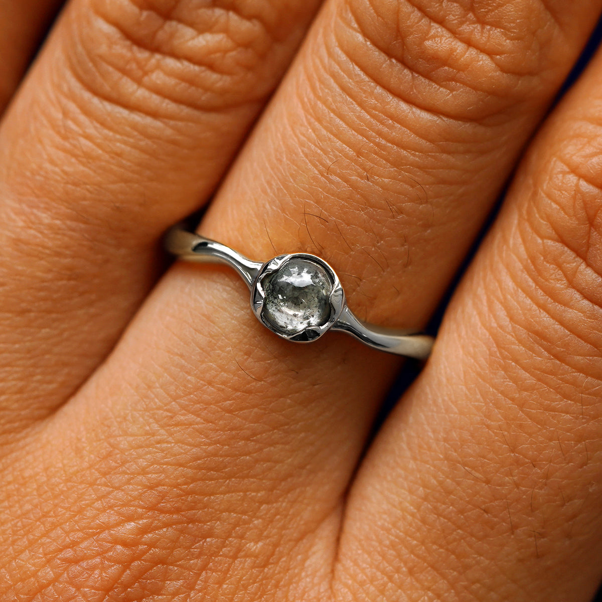 Close up view of a model's hand wearing a 14k white gold round cabochon salt and pepper diamond ring
