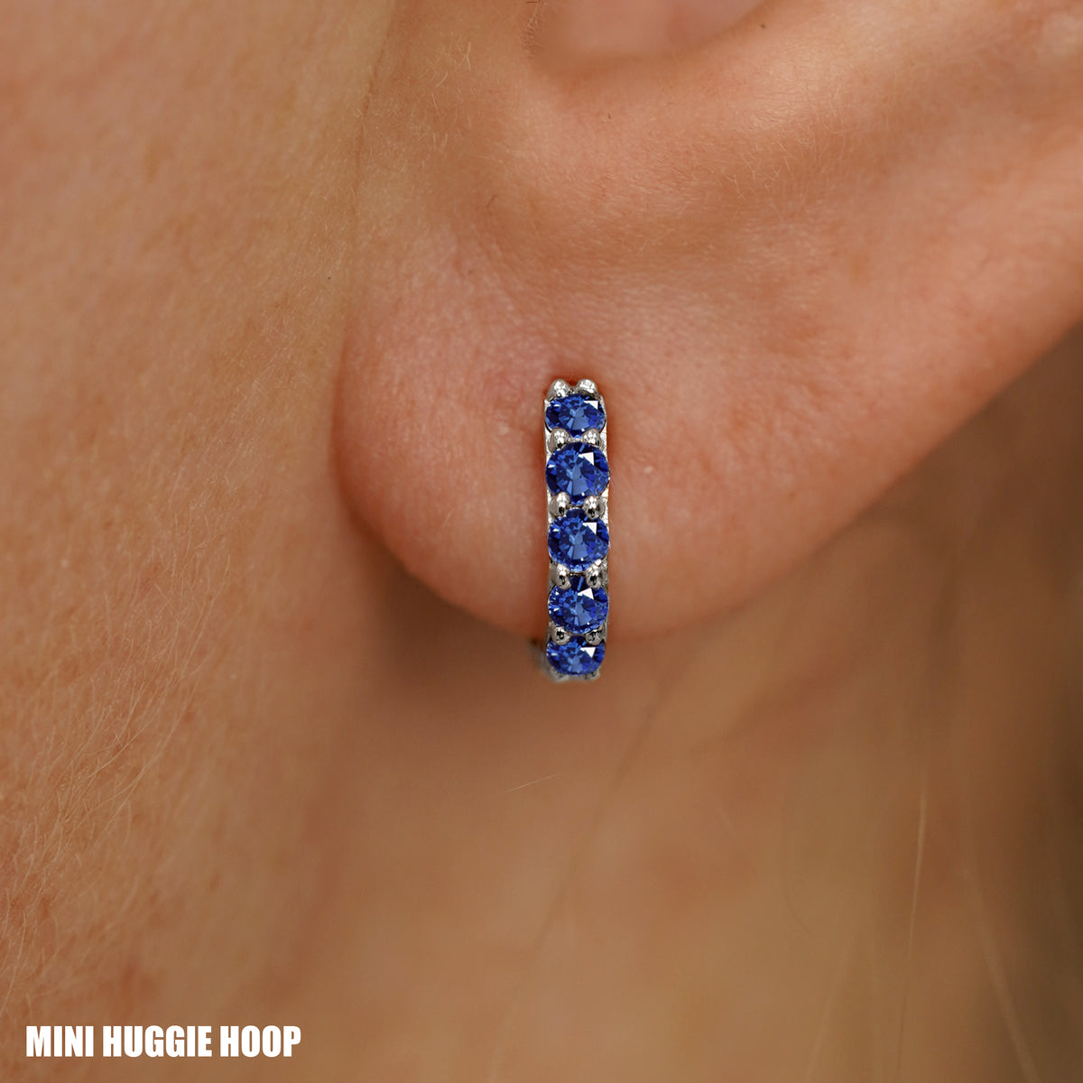 Close up view of a model's ear wearing a white gold Mini Blue Sapphire Huggie Hoop