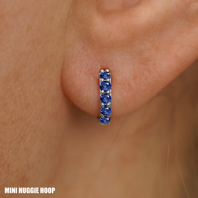 Close up view of a model's ear wearing a white gold Mini Blue Sapphire Huggie Hoop