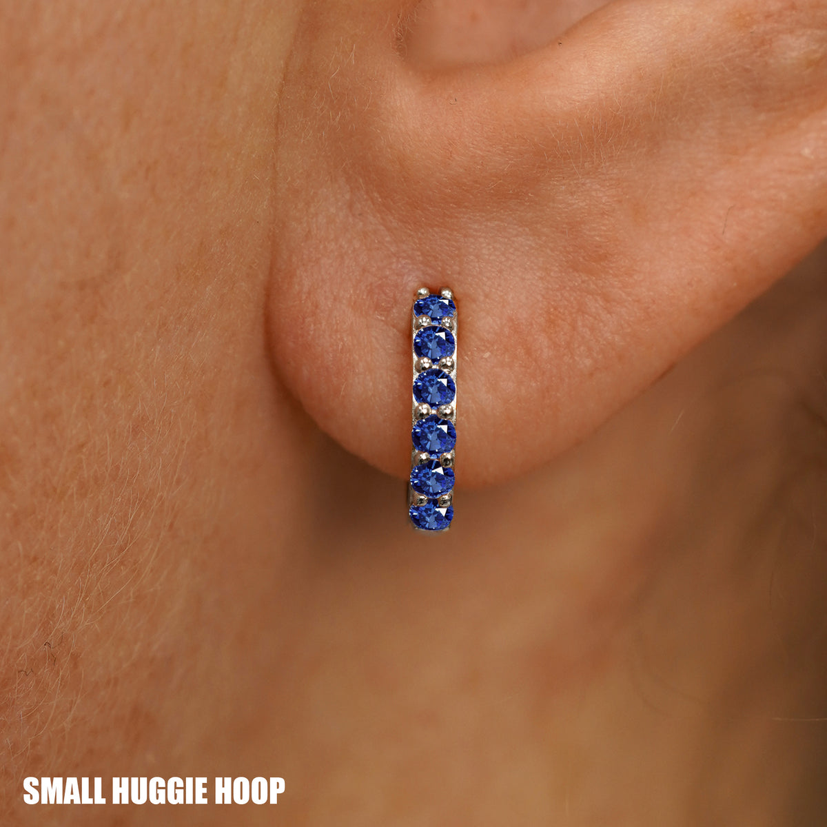 Close up view of a model's ear wearing a white gold Small Blue Sapphire Huggie Hoop
