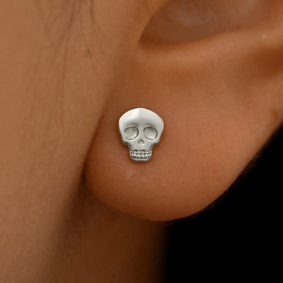 Close up view of a model's ear wearing a 14k white gold Skull Earring