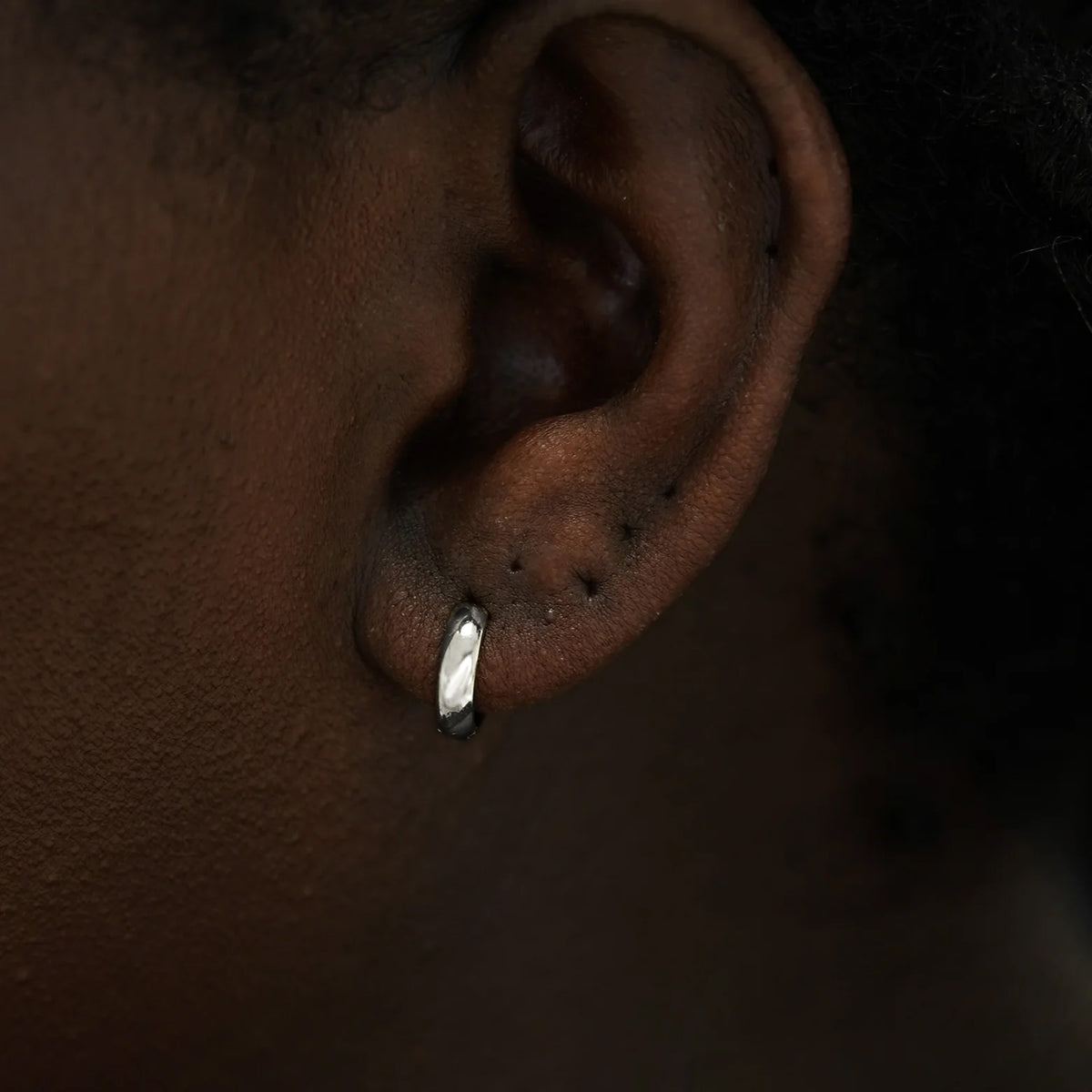 Close up view of a model's ear wearing a 14k white gold Small Wide Huggie Hoop Earring