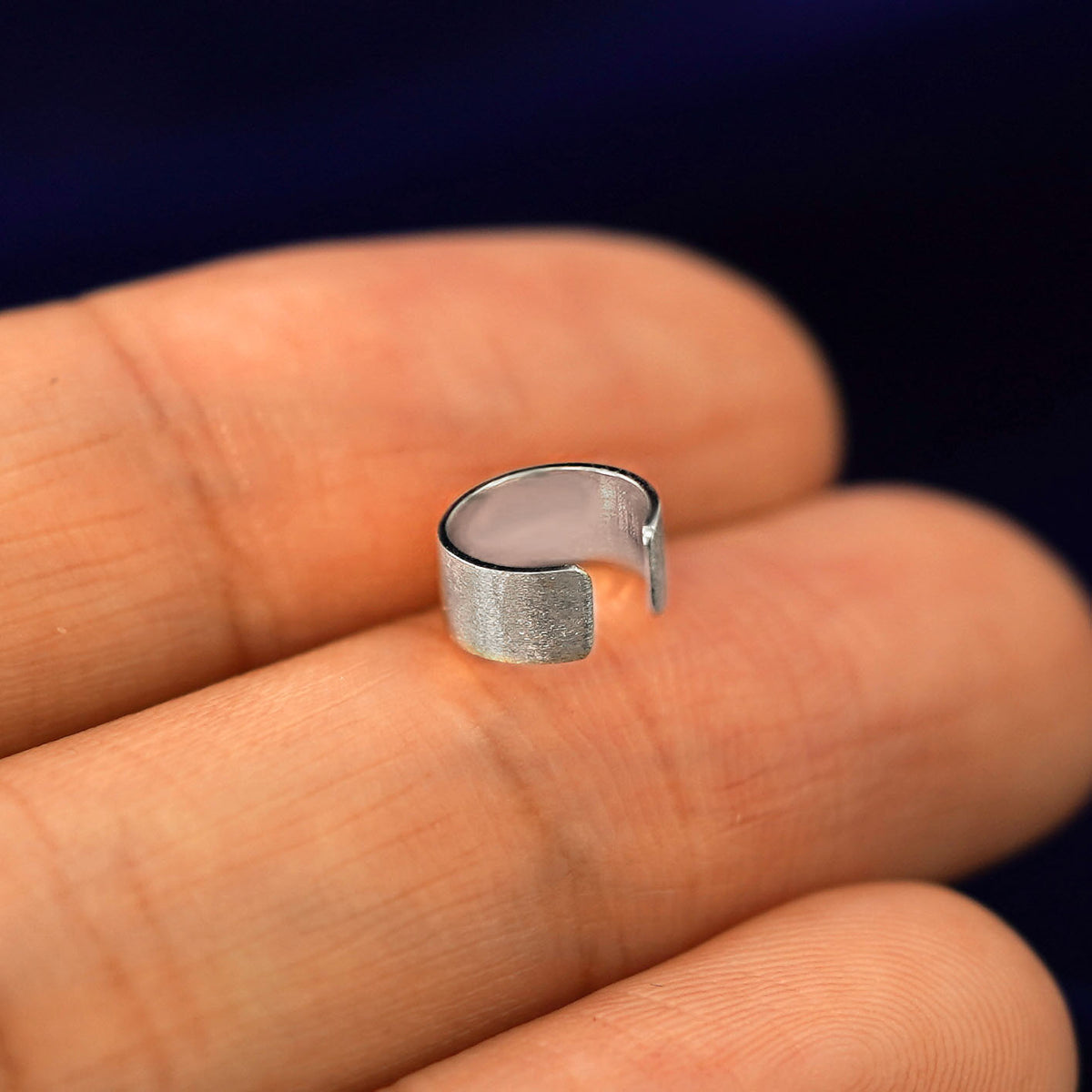 A solid white gold Thick Stardust Cuff earring resting on a model's fingertips