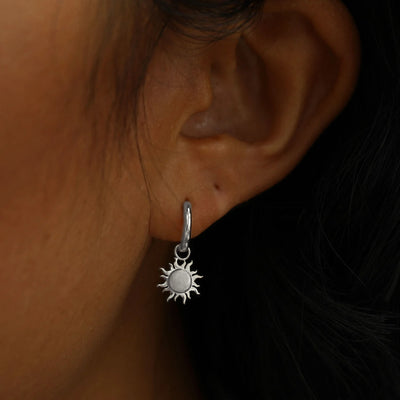 Close up view of a model's ear wearing a white gold Sun Charm on a Curvy Huggie Hoop