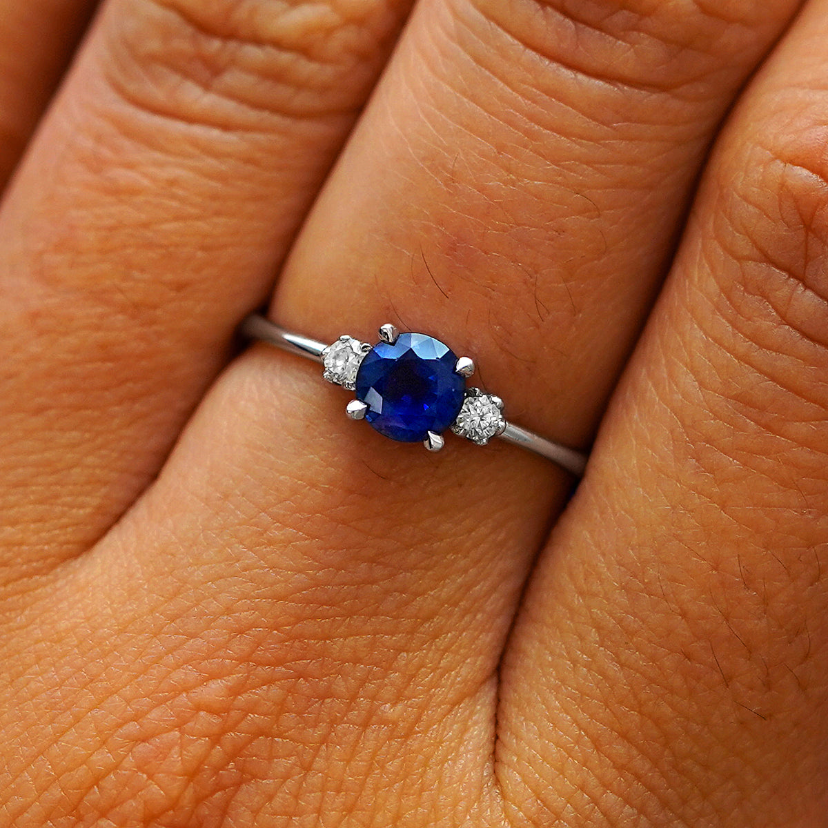 Close up view of a model's hand wearing a 14k white gold three stone sapphire ring
