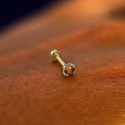 A solid 14k white gold Tiger Eye Flatback Piercing resting on the back of a model's hand