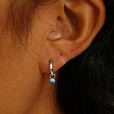 Close up view of a model's ear wearing a white gold Turquoise Charm on a Curvy Huggie Hoop