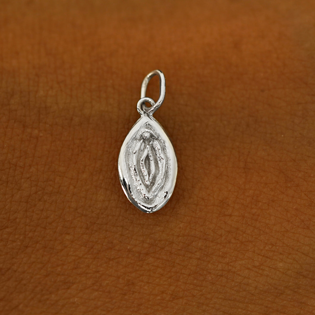 A solid 14k white gold Vulva Charm resting on the back of a model's hand