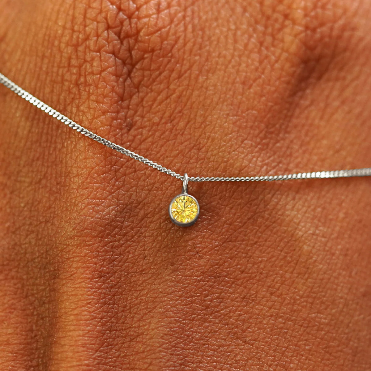 Close up view of a 14k white gold Yellow Diamond Necklace draped across the back of a model's hand