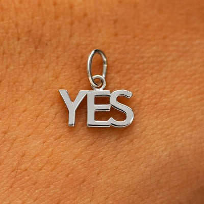 A solid 14k white gold Yes Charm on the back of a models hand