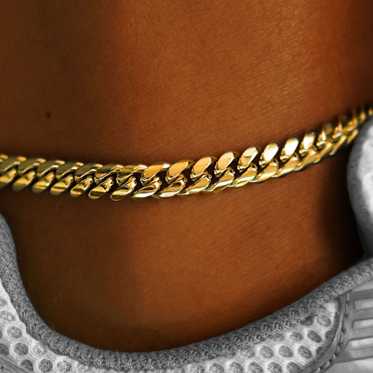 Close up view of a model's ankle wearing a yellow gold Miami Cuban Anklet