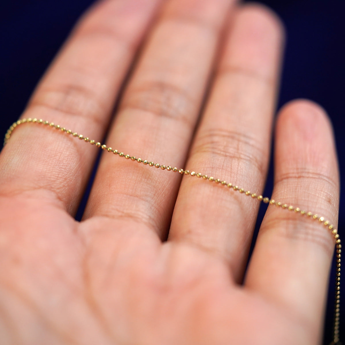 A yellow gold Bead Bracelet resting on a model's fingers