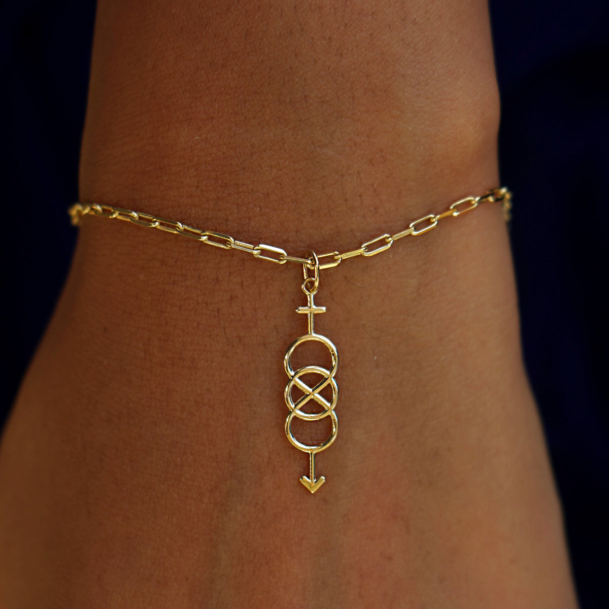 A model's wrist wearing a yellow gold Bisexual Symbol Charm on a Butch Bracelet