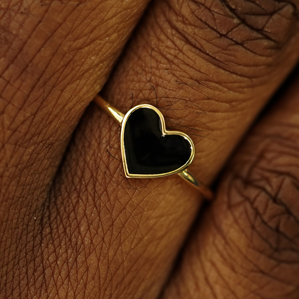 Close up view of a model's fingers wearing a 14k yellow gold black enamel heart ring
