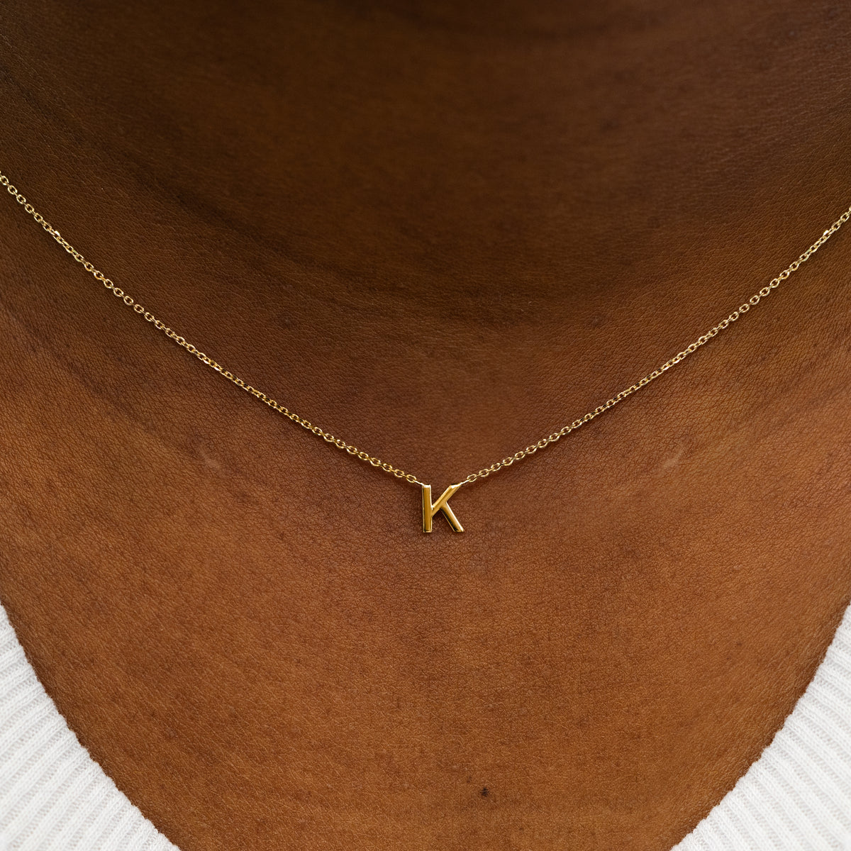 Close up view of a model's neck wearing a 14k solid yellow gold Block Initial Necklace in the letter K