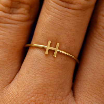 Close up view of a model's fingers wearing a 14k yellow gold block initial Ring with the letter H