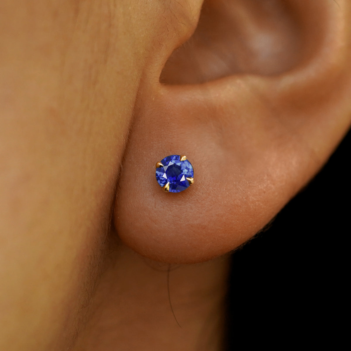 A model's ear wearing a solid 14k yellow gold blue sapphire pressure lock stud earring
