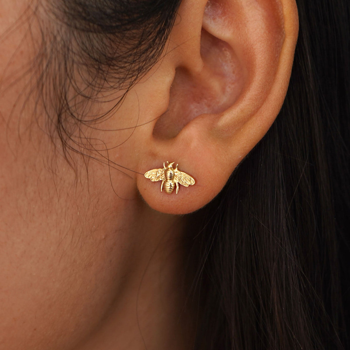 Close up view of a model's ear wearing a yellow gold Bee Earring