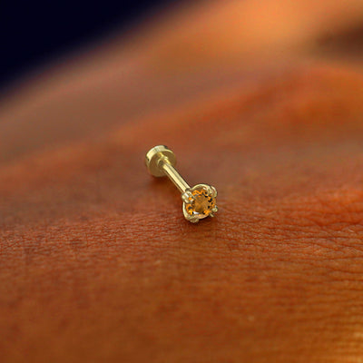 A solid 14k yellow gold Citrine Flatback Piercing resting on the back of a model's hand