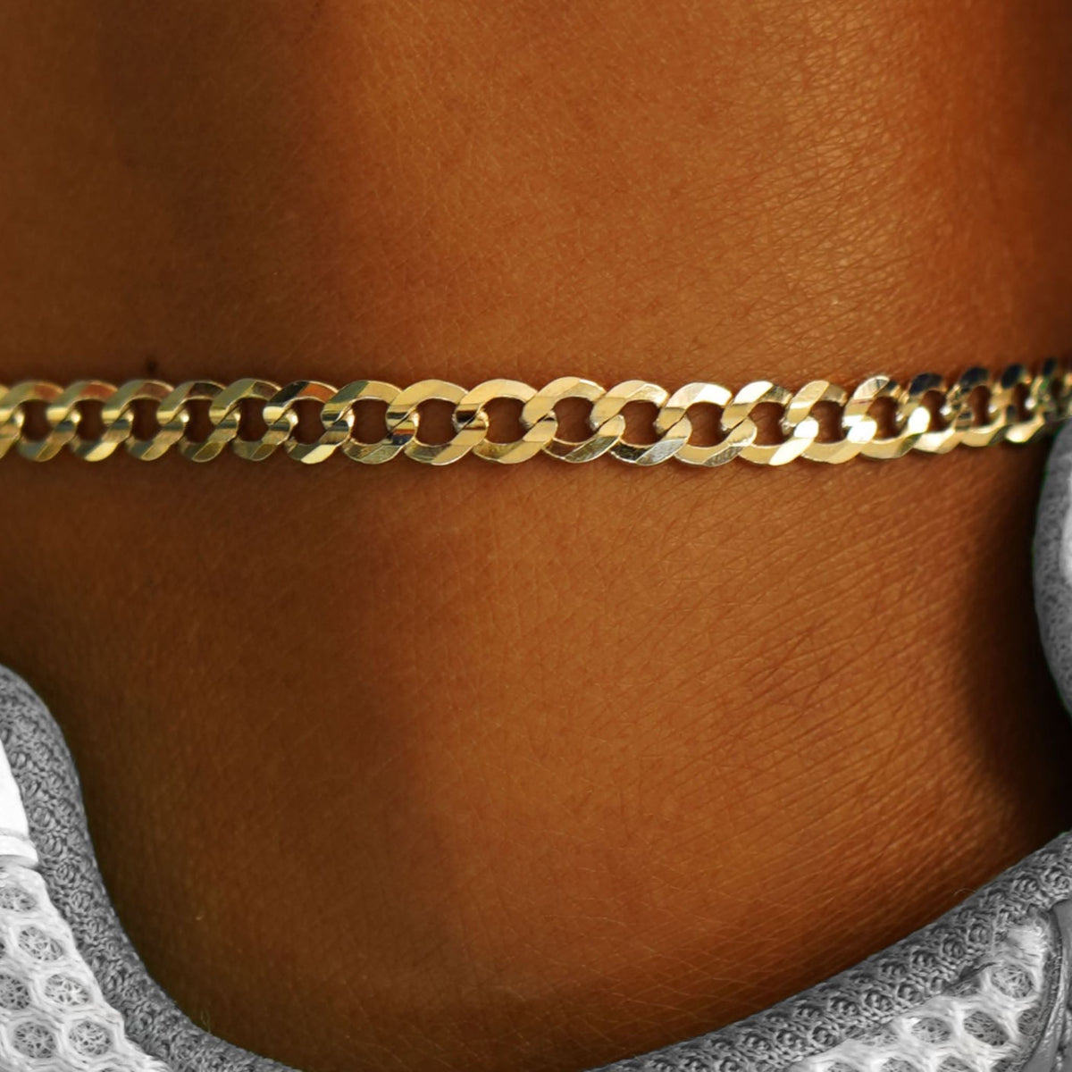 Close up view of a model's ankle wearing a 14k yellow gold Curb Anklet