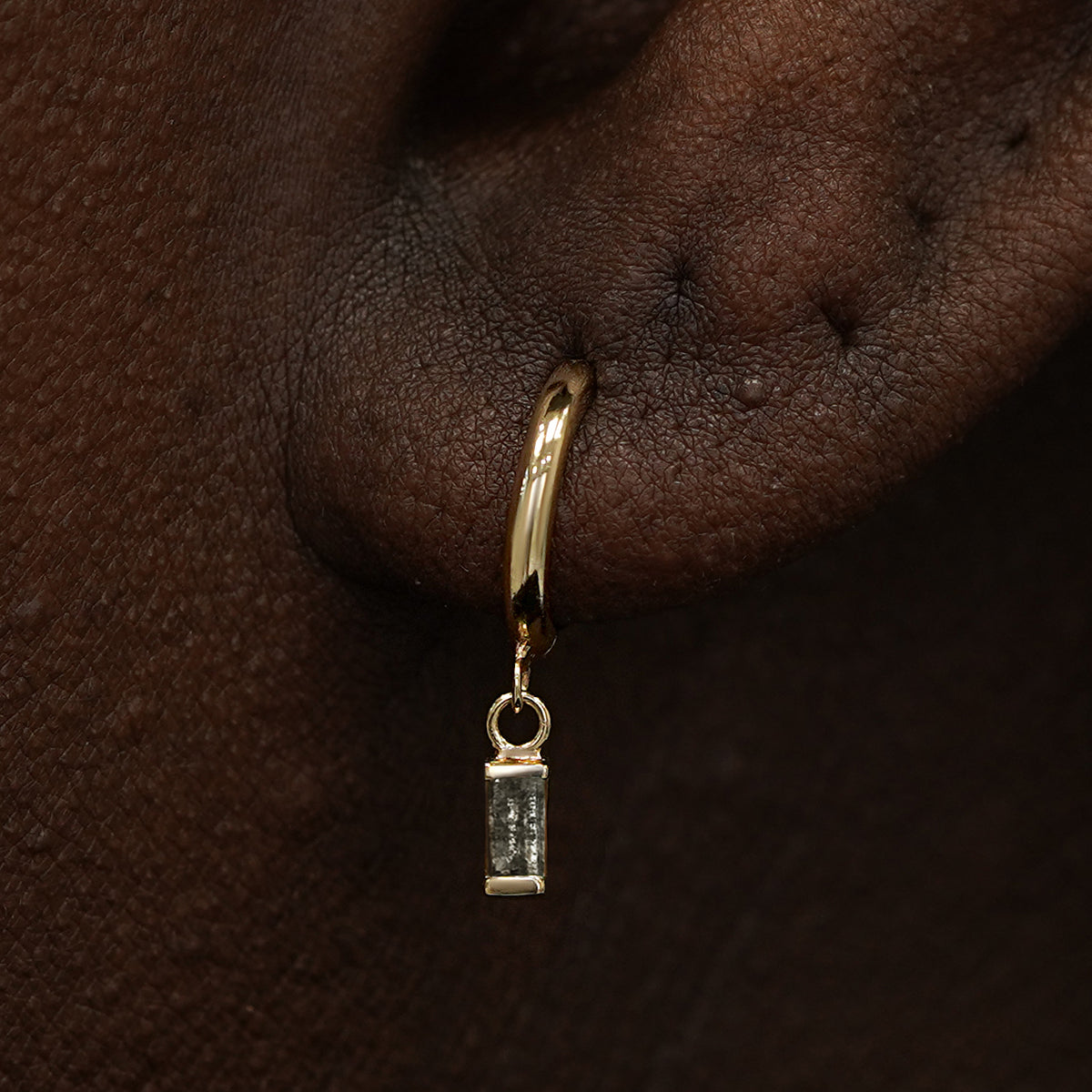 Close up view of a model's ear wearing a yellow gold Baguette Diamond Dangle Huggie Hoop