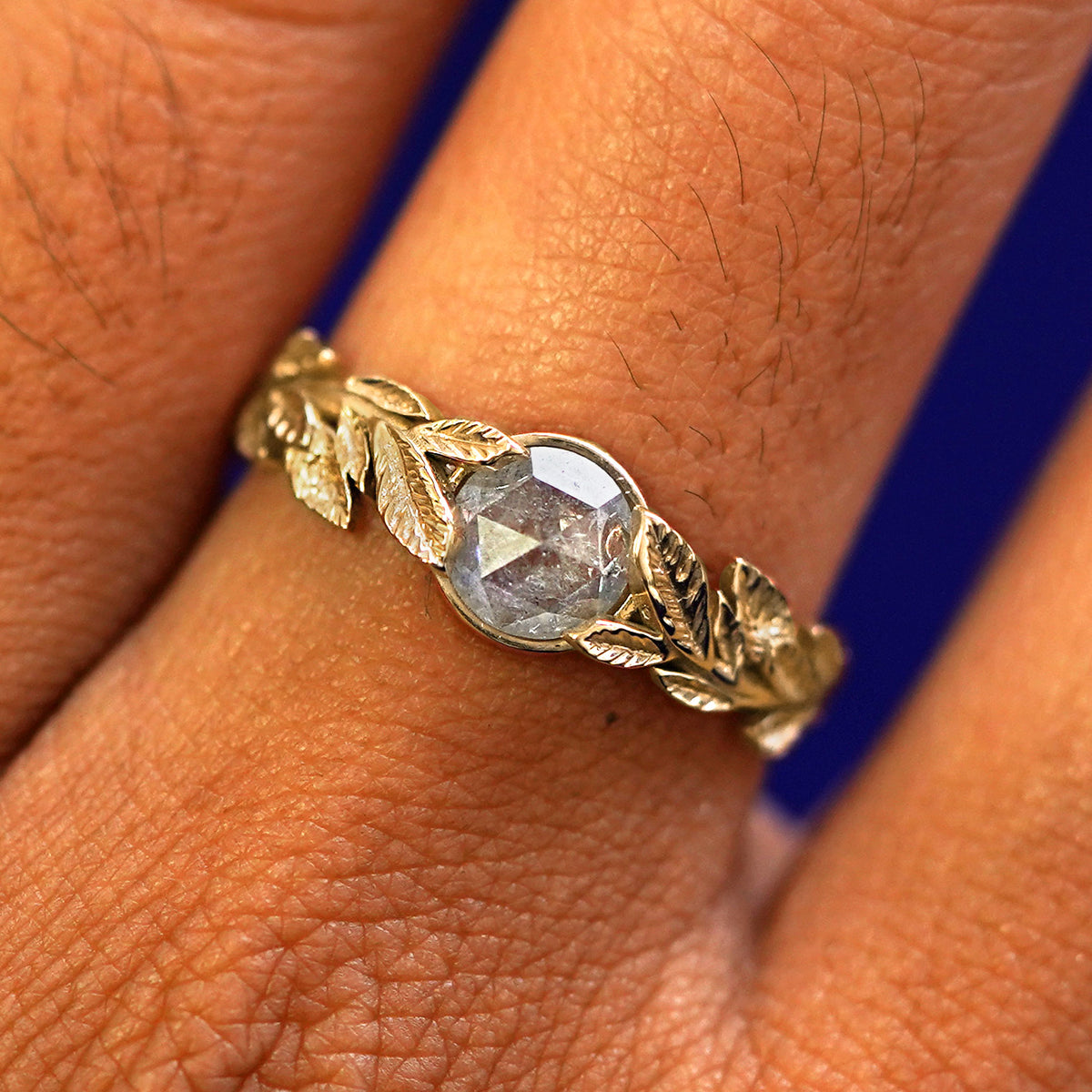 Close up view of a model's fingers wearing a 14k yellow gold Salt and Pepper Diamond Leaves Ring