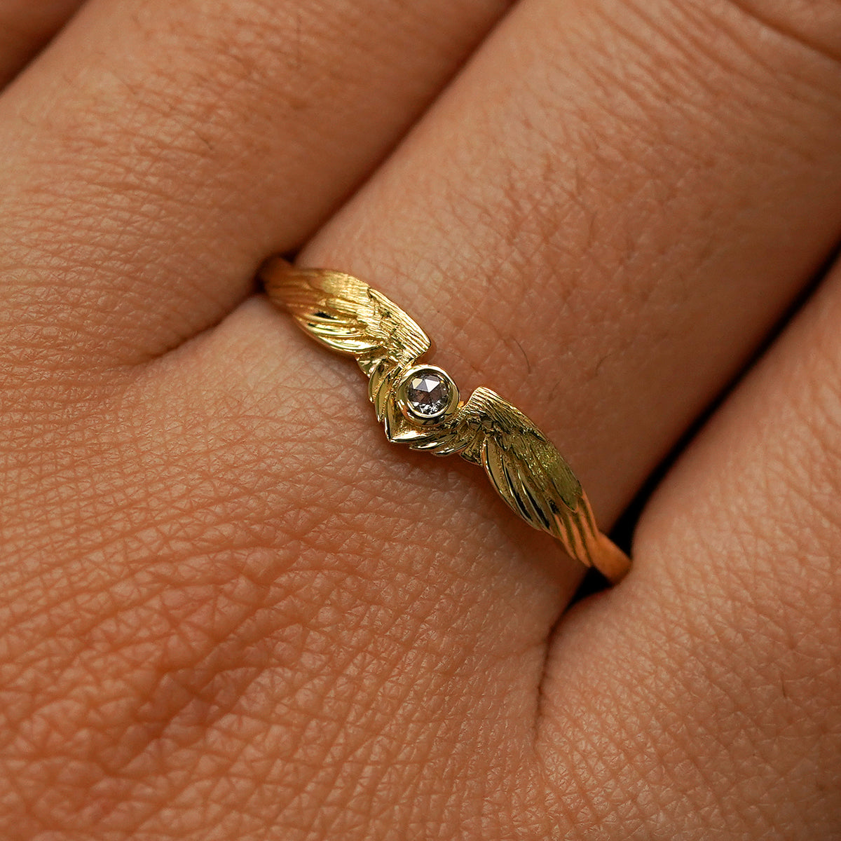 Close up view of a model's fingers wearing a 14k yellow gold Salt and Pepper Diamond Wings Ring