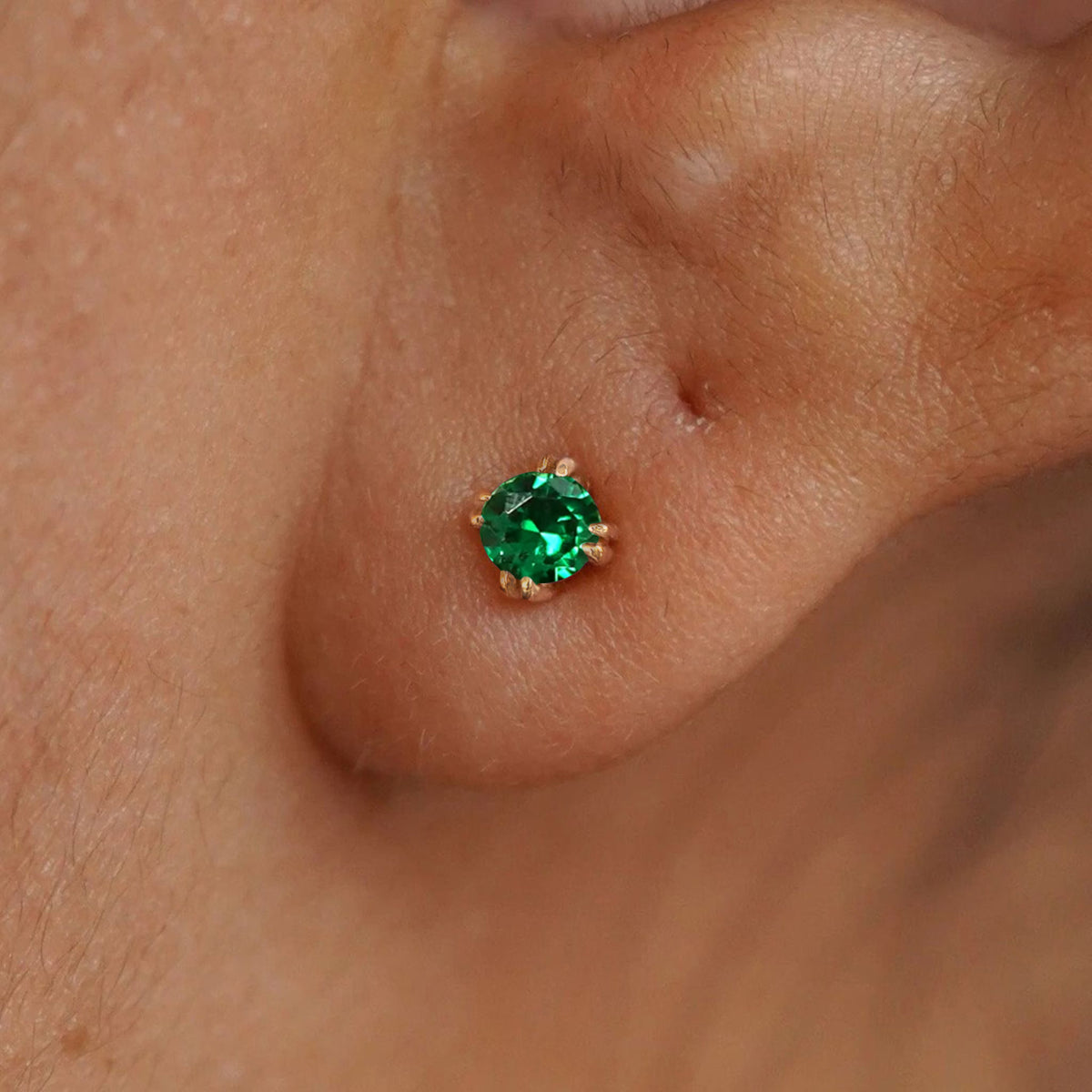 Close up view of a model's ear wearing a 14k yellow gold Emerald Earring